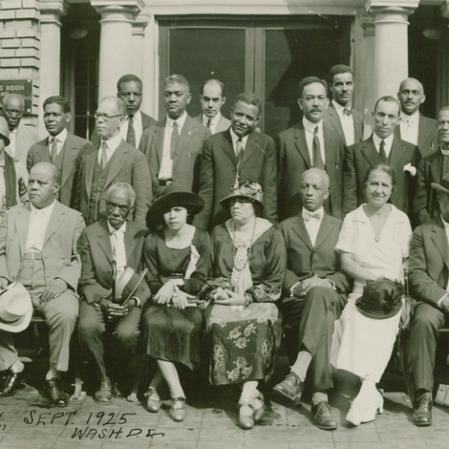 A group of well-dressed men and women pose for a photo on steps in front of a building, dated September 1925 in Washington, D.C. Like fashion-forward entrepreneurs at a Shopify launch party, they exude confidence and style, dressed in suits and dresses with some wearing hats.